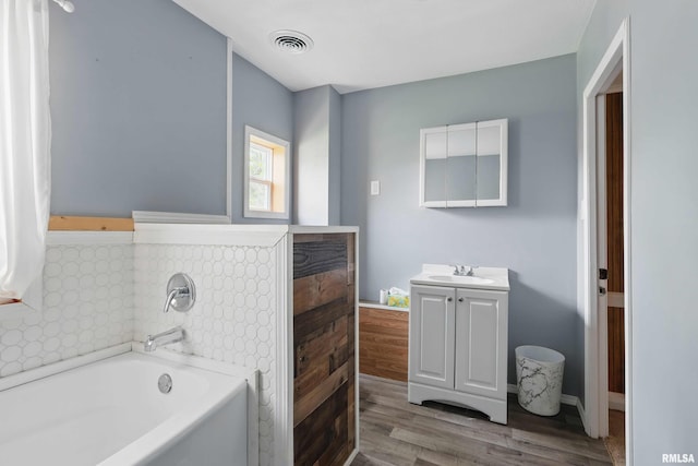 bathroom featuring visible vents, a bath, wood finished floors, and vanity