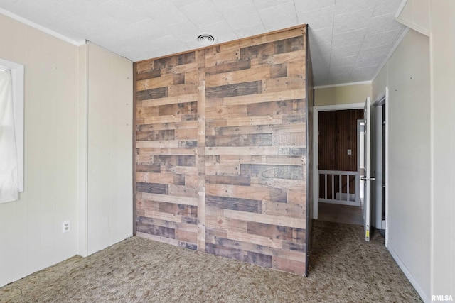 unfurnished room with crown molding, carpet, wood walls, and visible vents