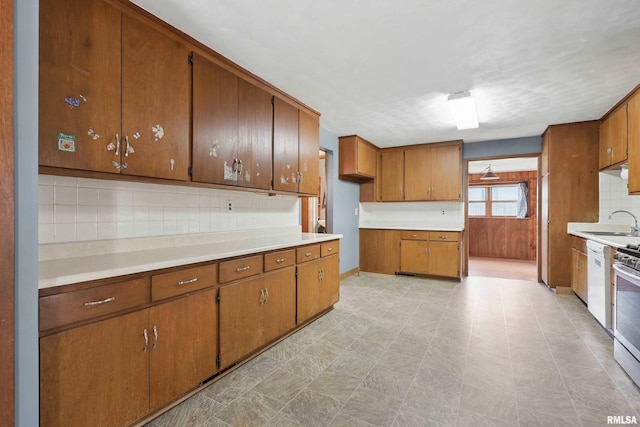 kitchen featuring brown cabinetry, white dishwasher, light countertops, a sink, and backsplash