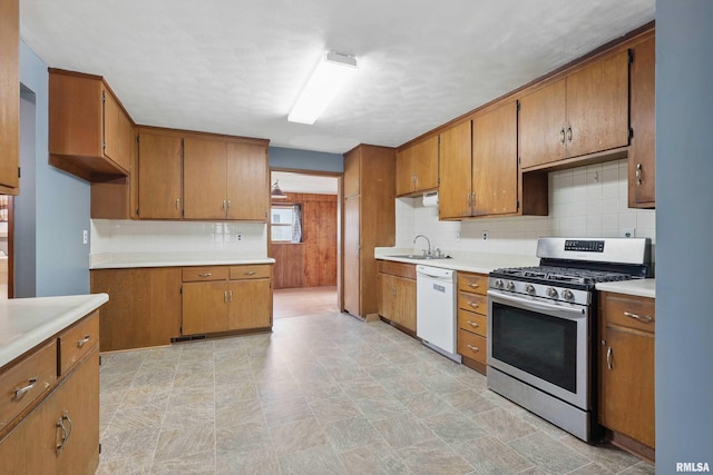 kitchen with brown cabinetry, dishwasher, stainless steel gas range, a sink, and backsplash