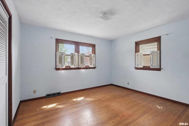 empty room with light wood-style floors, baseboards, and visible vents