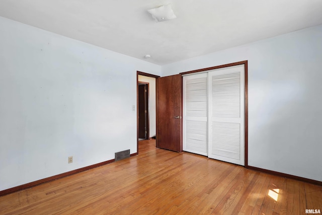 unfurnished bedroom with baseboards, a closet, light wood finished floors, and visible vents