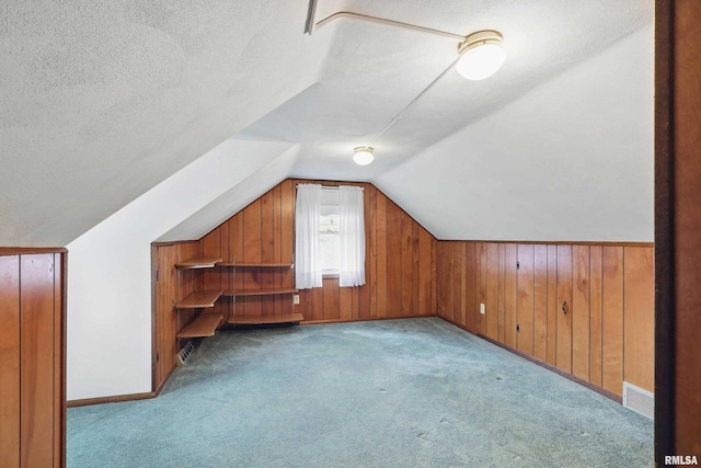 additional living space featuring wooden walls, a textured ceiling, carpet, lofted ceiling, and visible vents