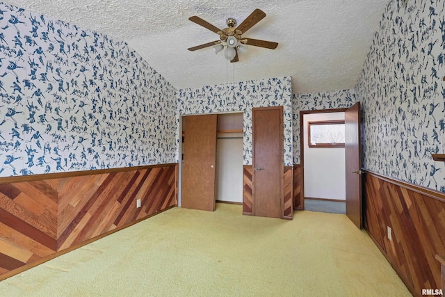 unfurnished bedroom with carpet, a textured ceiling, a wainscoted wall, and wallpapered walls
