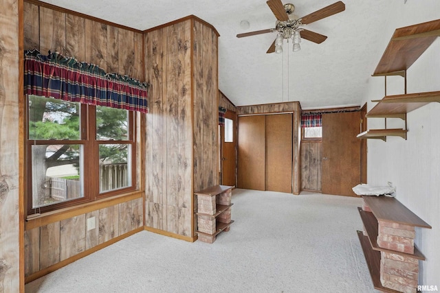 interior space featuring wood walls, carpet, a ceiling fan, baseboards, and lofted ceiling