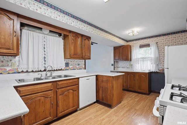 kitchen featuring a sink, white appliances, brown cabinetry, wallpapered walls, and light wood-type flooring
