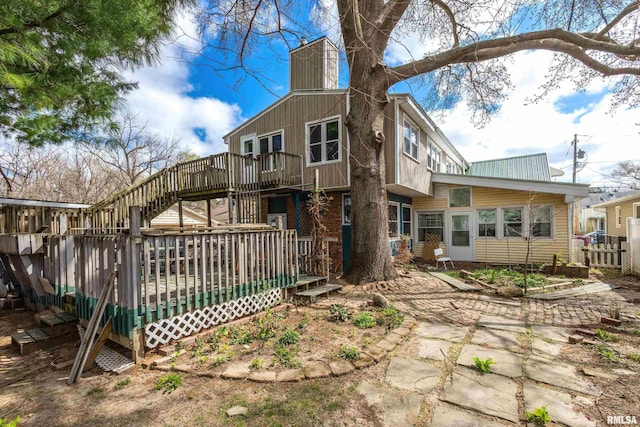 rear view of house featuring fence, a deck, a patio, a chimney, and stairs