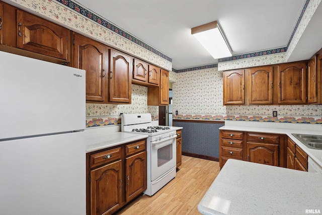 kitchen featuring white appliances, light countertops, brown cabinetry, light wood-style flooring, and wallpapered walls