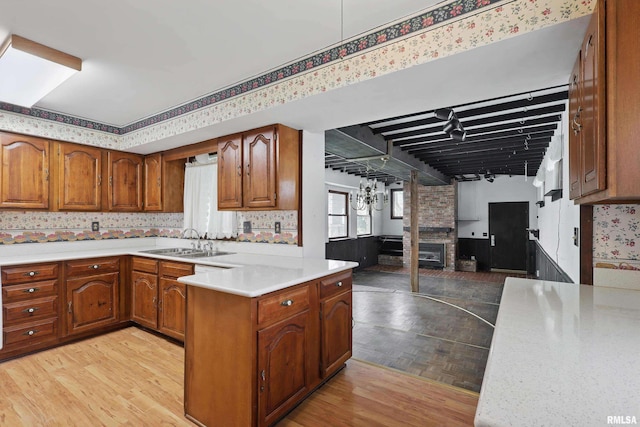 kitchen with a sink, brown cabinets, wallpapered walls, and light countertops