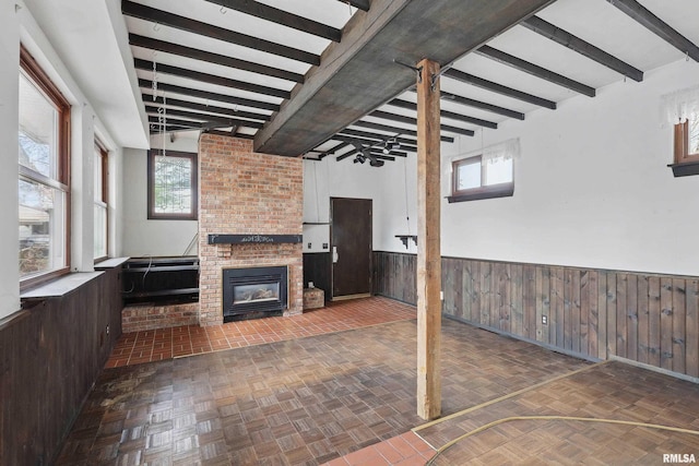 basement with wooden walls, a brick fireplace, a healthy amount of sunlight, and a wainscoted wall