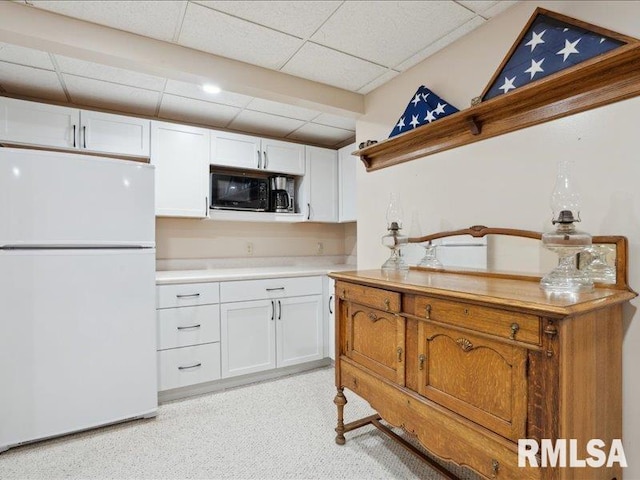 kitchen with black microwave, freestanding refrigerator, a drop ceiling, and white cabinetry