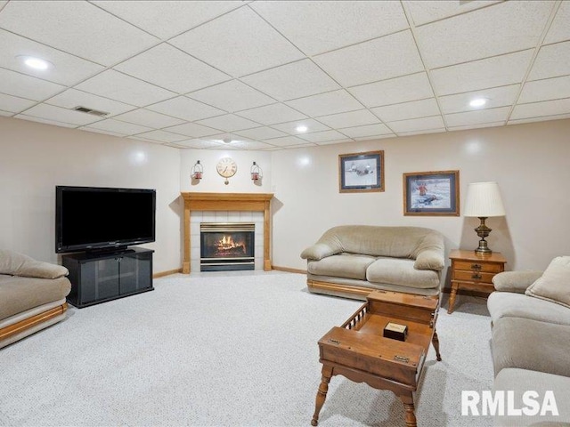 living room with carpet flooring, baseboards, a drop ceiling, and a tile fireplace