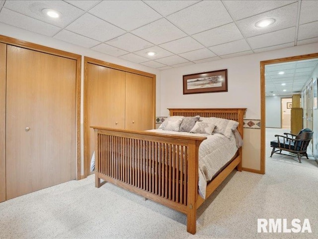 carpeted bedroom with multiple closets, a drop ceiling, and recessed lighting