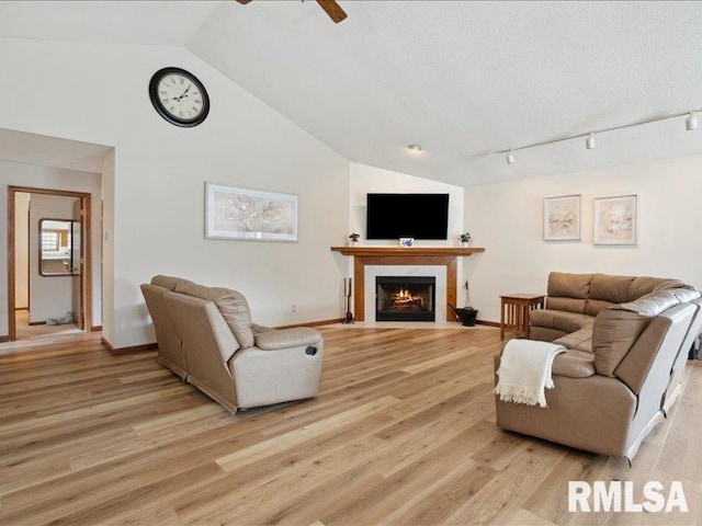 living area featuring a ceiling fan, vaulted ceiling, a fireplace with flush hearth, and light wood finished floors