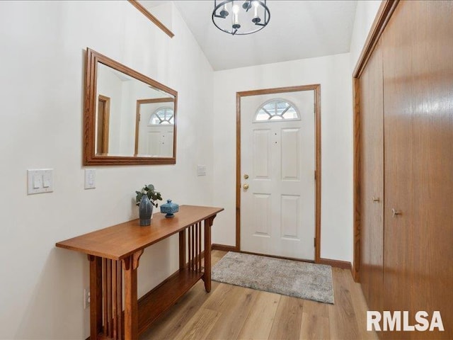 entryway featuring baseboards, light wood finished floors, lofted ceiling, and an inviting chandelier