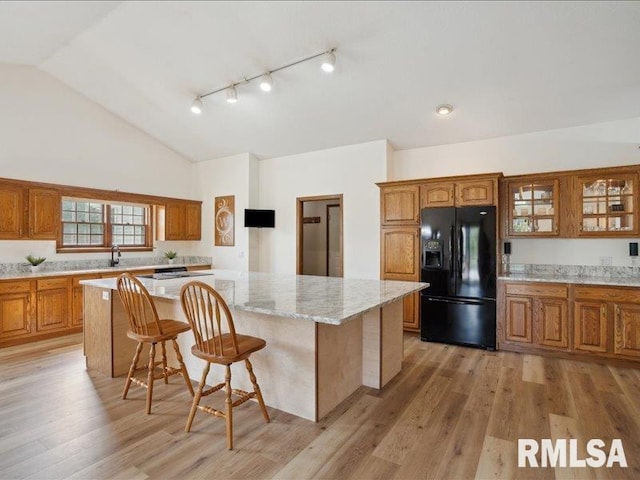 kitchen with brown cabinets, a center island, a kitchen bar, glass insert cabinets, and black fridge with ice dispenser