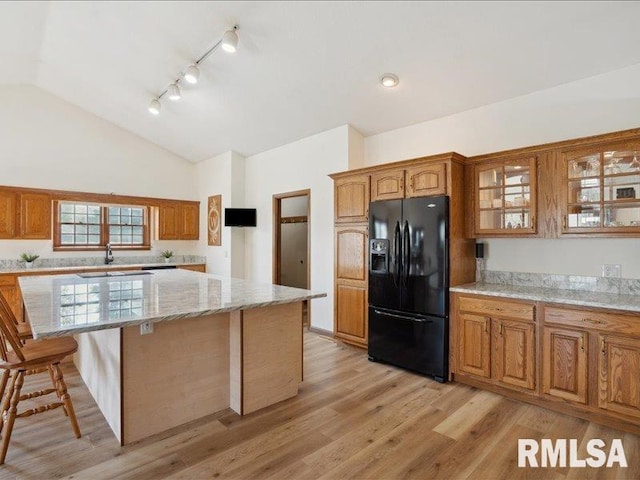 kitchen with brown cabinetry, black refrigerator with ice dispenser, vaulted ceiling, and glass insert cabinets