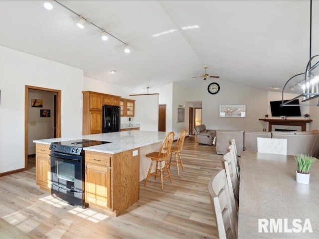kitchen featuring open floor plan, vaulted ceiling, light wood-style flooring, and black appliances