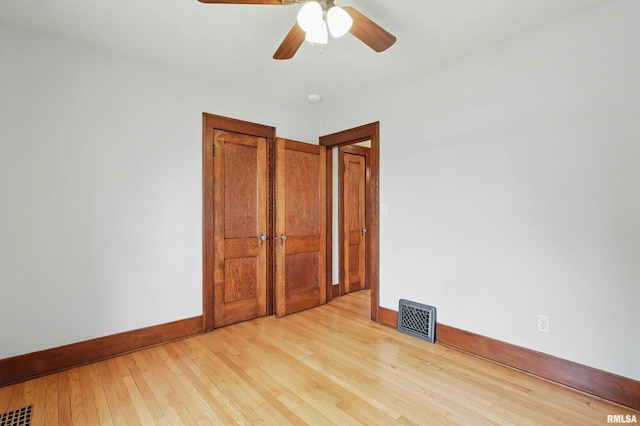 empty room with baseboards, a ceiling fan, light wood finished floors, and visible vents