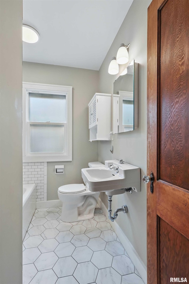 bathroom featuring baseboards, tile patterned floors, toilet, and a bath