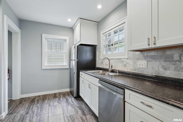 kitchen with dark countertops, a sink, stainless steel appliances, white cabinetry, and decorative backsplash