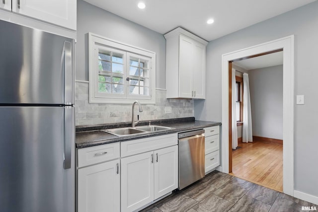 kitchen featuring white cabinets, dark countertops, appliances with stainless steel finishes, a sink, and backsplash