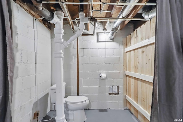 bathroom featuring finished concrete flooring, concrete block wall, and toilet