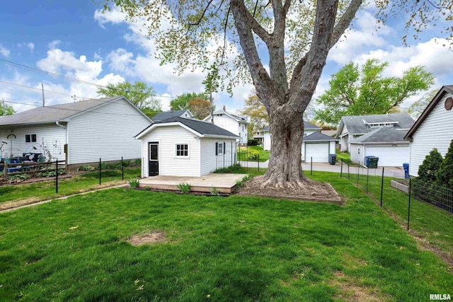 back of property with fence, a detached garage, a wooden deck, and a lawn