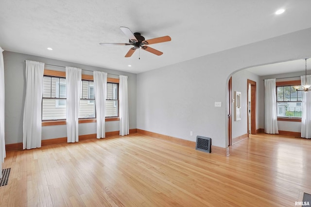 empty room featuring visible vents, light wood-style floors, baseboards, arched walkways, and ceiling fan with notable chandelier