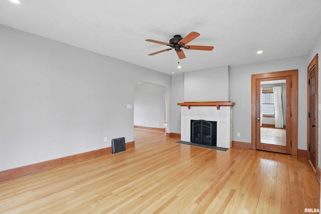 unfurnished living room featuring hardwood / wood-style floors, ceiling fan, recessed lighting, a tile fireplace, and arched walkways