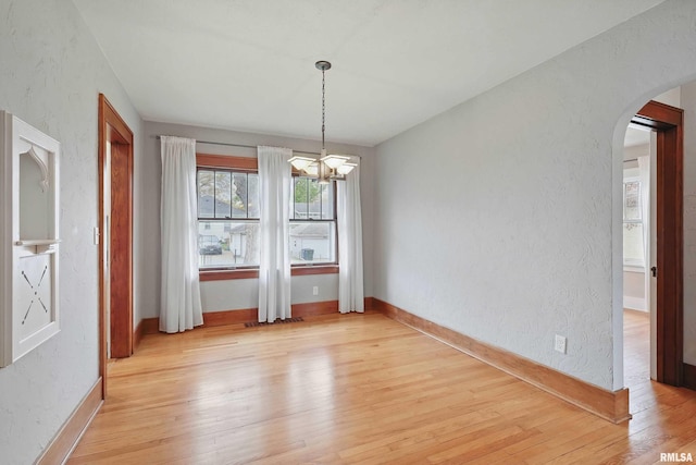 unfurnished dining area featuring arched walkways, baseboards, a chandelier, and light wood-style floors