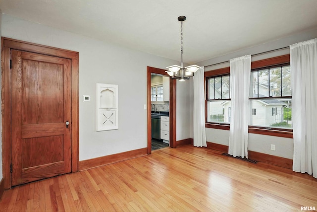 unfurnished dining area featuring baseboards, light wood-style floors, a notable chandelier, and visible vents