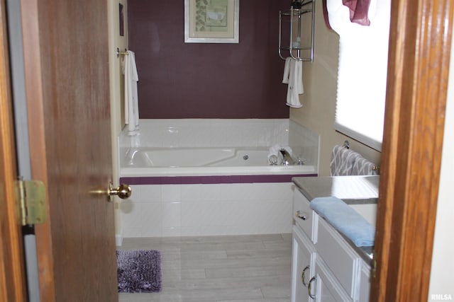 full bath featuring a relaxing tiled tub, wood finished floors, and vanity