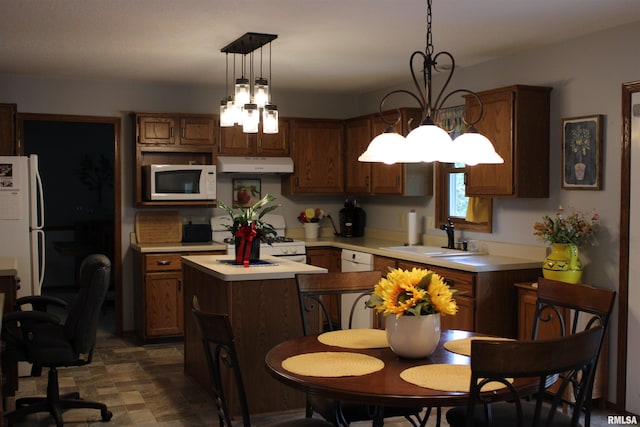kitchen with a sink, light countertops, a chandelier, under cabinet range hood, and white appliances