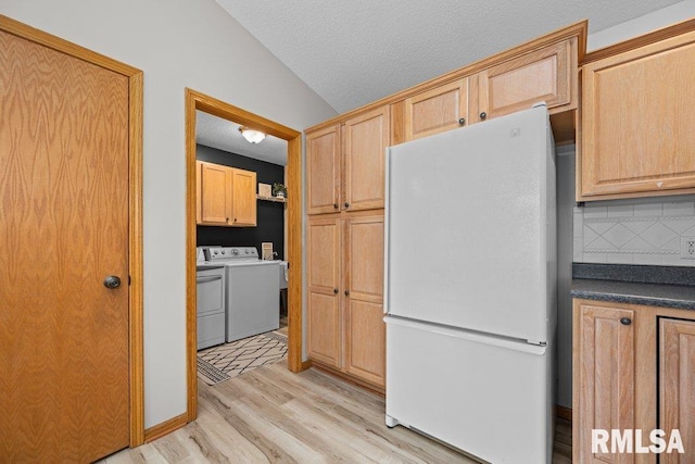 kitchen with washer and dryer, dark countertops, freestanding refrigerator, light wood-type flooring, and backsplash