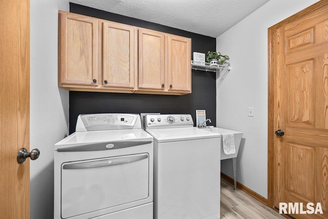 clothes washing area with a textured ceiling, light wood-type flooring, cabinet space, baseboards, and separate washer and dryer