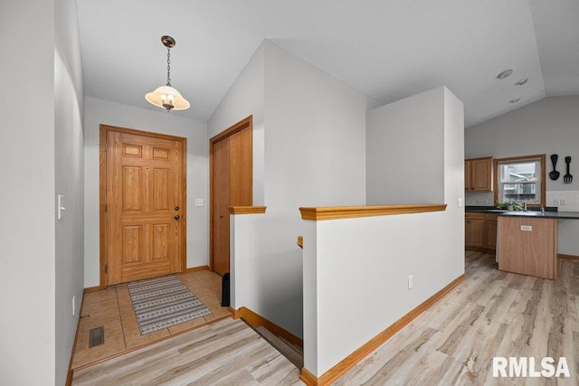 foyer featuring baseboards, light wood finished floors, lofted ceiling, and visible vents