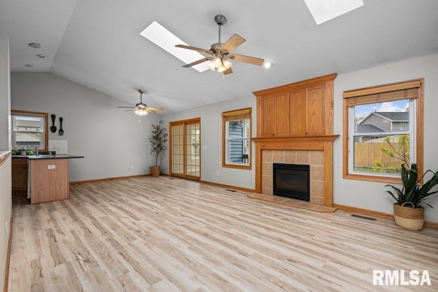 unfurnished living room with a ceiling fan, a skylight, visible vents, and a tile fireplace