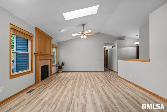 unfurnished living room featuring visible vents, baseboards, lofted ceiling with skylight, a tile fireplace, and light wood finished floors