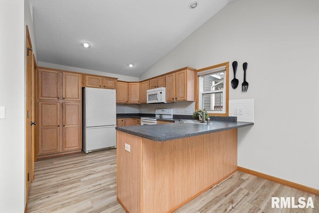 kitchen with a peninsula, white appliances, light wood-style floors, a sink, and vaulted ceiling