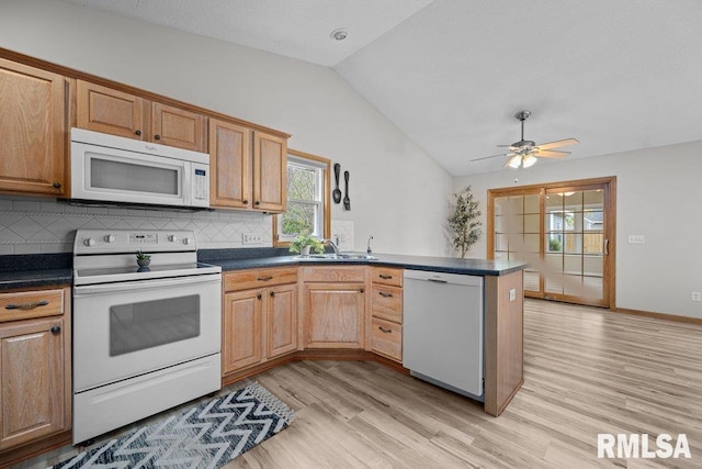 kitchen featuring a peninsula, dark countertops, white appliances, light wood-type flooring, and vaulted ceiling