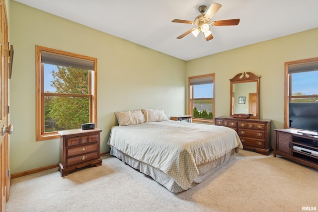 bedroom featuring light colored carpet, baseboards, ceiling fan, and multiple windows