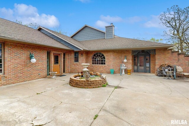rear view of house featuring brick siding, a shingled roof, a patio area, and a chimney