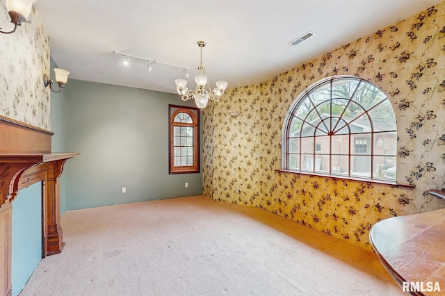 unfurnished dining area with visible vents, wallpapered walls, a chandelier, rail lighting, and carpet flooring