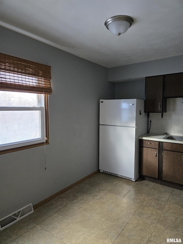 kitchen featuring backsplash, visible vents, light countertops, baseboards, and freestanding refrigerator