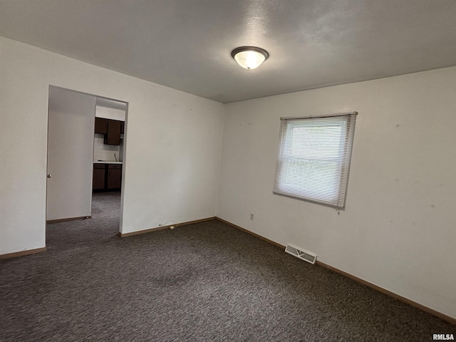 empty room featuring baseboards, visible vents, and dark carpet