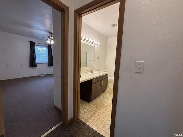 hallway featuring visible vents, a sink, baseboards, and light colored carpet