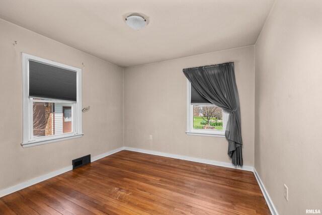 empty room featuring baseboards, visible vents, and hardwood / wood-style floors