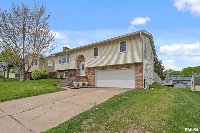 raised ranch with driveway, a chimney, brick siding, a front lawn, and an attached garage