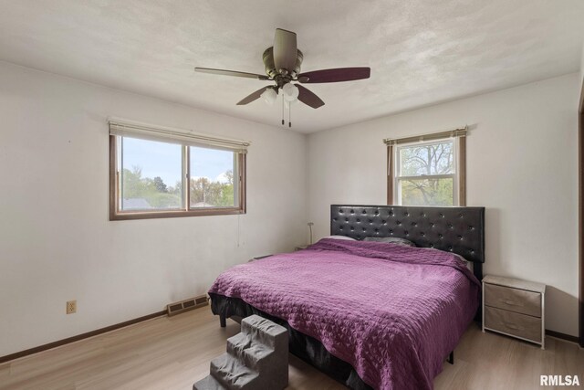 bedroom featuring baseboards, ceiling fan, light wood finished floors, and visible vents